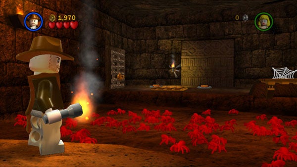 Lego Indiana Jones character in game scene with red spiders.Screenshot of Lego Indiana Jones video game with character and scorpions.