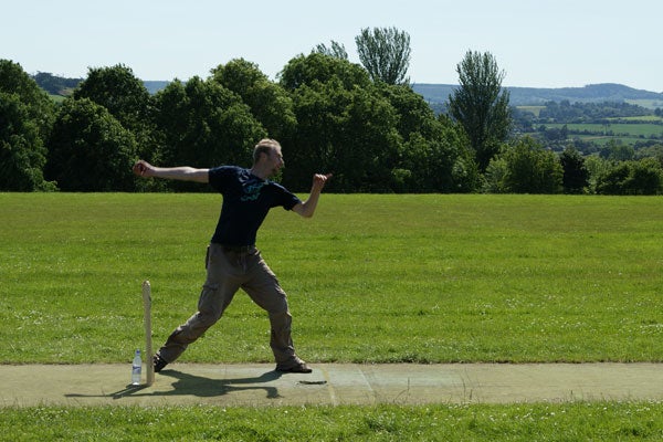 Man playing cricket in a sunny fieldMan cricket bowling in sunny, grassy field with trees in background