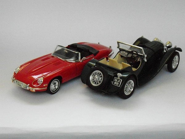 Red and black die-cast model cars on a gray background.Photo of two toy model cars on a white background.