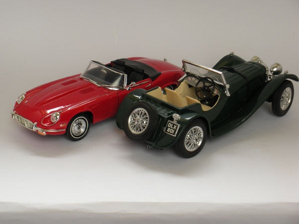 Two model cars, a red and a green one, side by side.Red and green toy convertible cars on white background