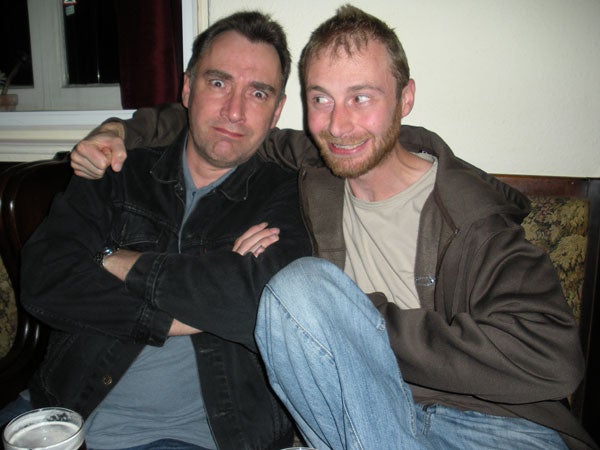 Two men sitting and smiling inside a room.Two men smiling and posing for the camera indoors.