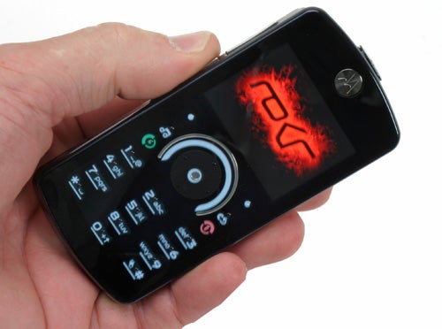 Hand holding a Motorola ROKR E8 phone with screen display on.