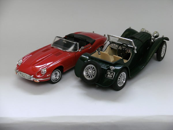 Two model cars, a red and a green one, on a white surface.Two vintage model cars on a white surface.