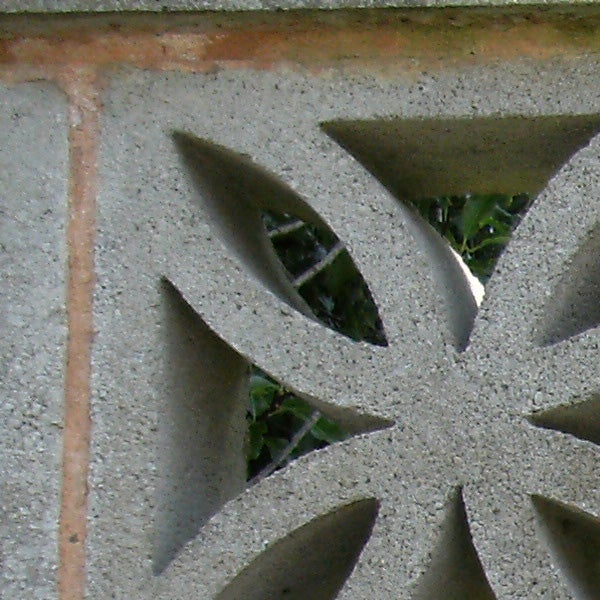 Close-up of decorative concrete block pattern with foliage background.Concrete wall decorative cut-out detail with foliage background.