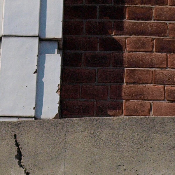 Close-up of a building corner showing brick and siding textures.Close-up of a brick wall with a cracked corner.
