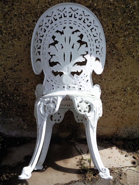 White ornate cast iron chair against a concrete wallOrnate white metal garden chair against a wall.