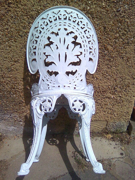White ornate metal chair against a wall.Intricate white metal chair against a wall.
