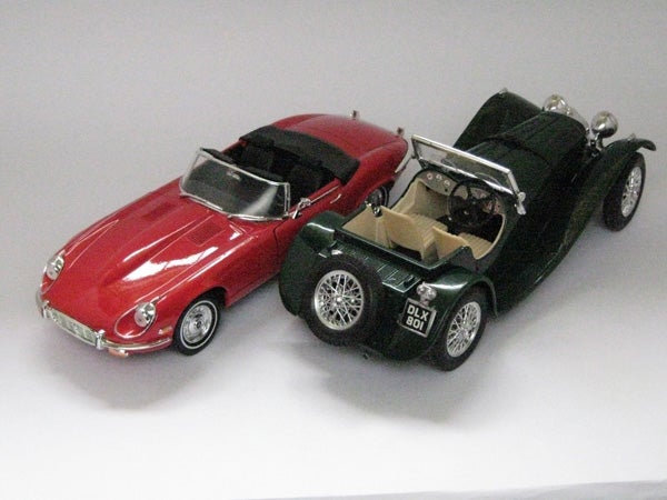 Photo of two toy model cars on a white surface.Photo of two model cars, red and green, on a white surface.