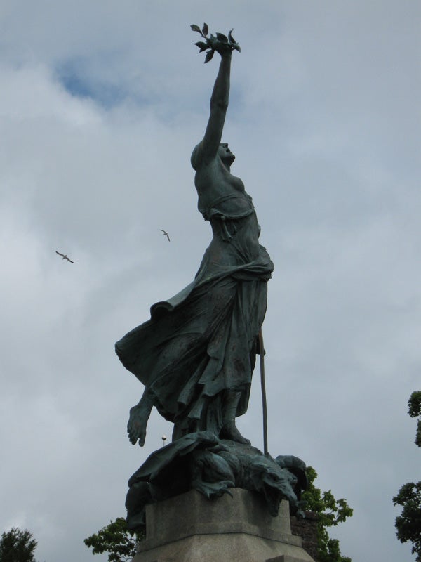 Statue reaching upwards with birds flying in the background.Statue of a female figure with a raised arm against the sky.