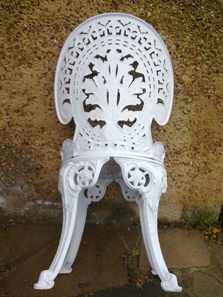 White ornate cast iron garden chair against a wall.White intricately designed cast iron chair against a wall.