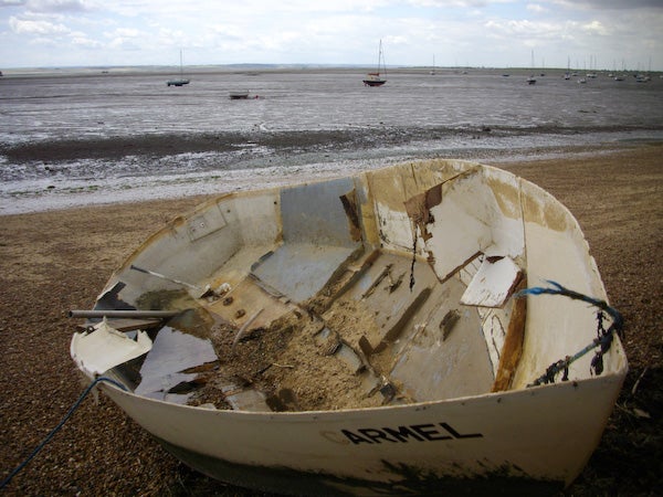 Damaged boat on shore with tide out and boats in distancePhotograph of an old boat on a beach taken with Pentax Optio E50.
