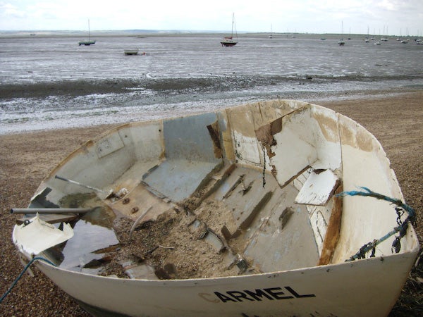 Damaged boat on shoreline with tide out.