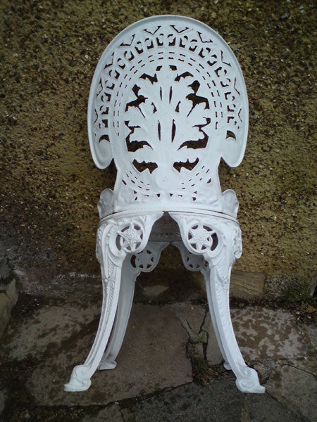 White ornate metal garden chair against a wallWhite ornate metal garden chair against a concrete wall.