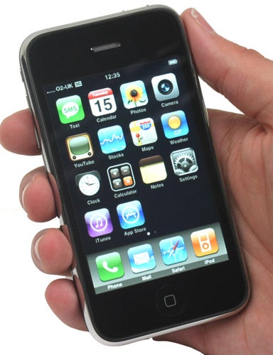 Hand holding an Apple iPhone 3G displaying home screen icons.