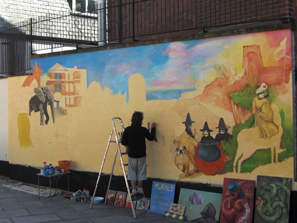 Photo of an artist painting a colorful mural on a wall.Artist painting colorful mural on urban wall.