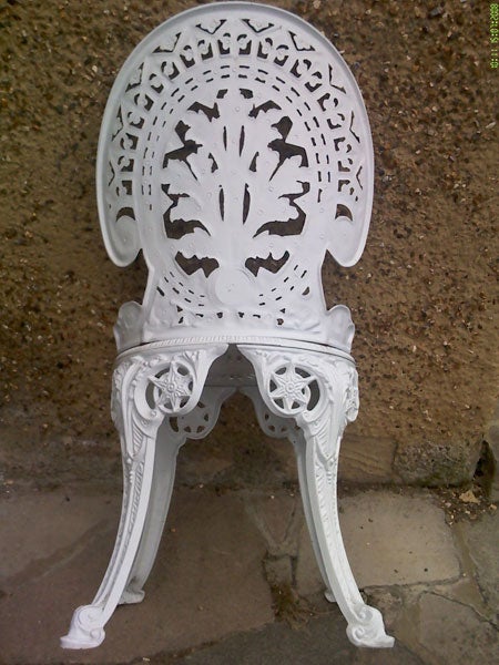 Ornate white cast iron garden chair against a wall.