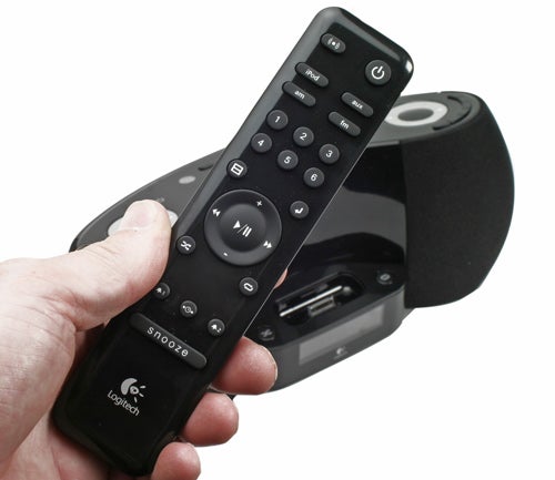 Hand holding Logitech Pure-Fi Dream remote control.Hand holding Logitech Pure-Fi Dream remote with speaker behind.