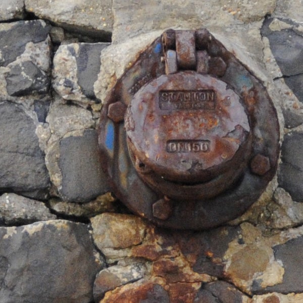 Rusty metal bolt on rocks captured in close-up.Rusty survey marker embedded in rock surface.