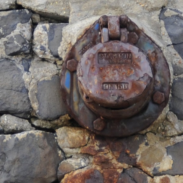 Close-up of rusted metal object on rocky surface.Rusty survey marker embedded in rocks.