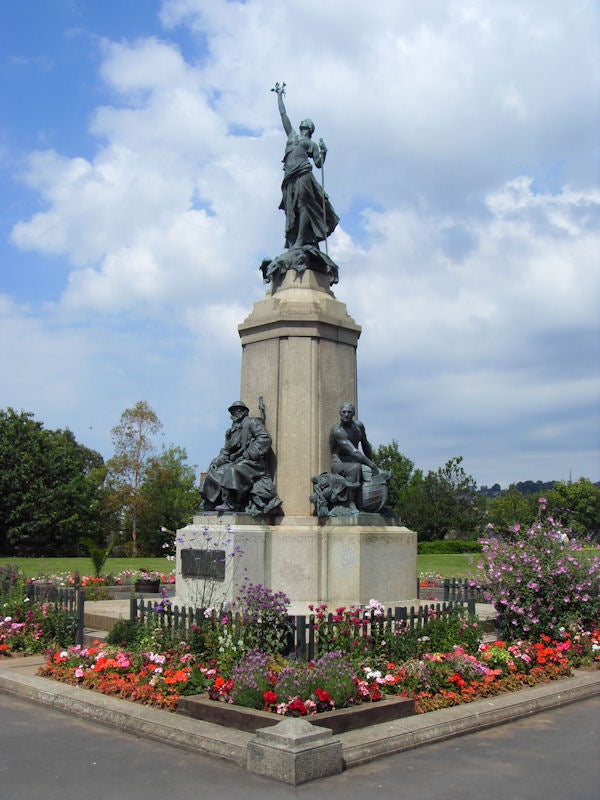 Statue surrounded by colorful flowerbeds under a blue skyStatue with flowers in a park on a sunny day.