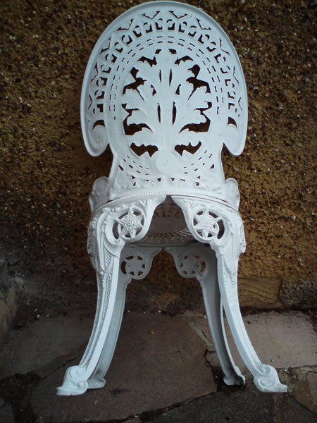 Ornate white garden chair against a textured wall.White ornate metal chair against a textured wall.