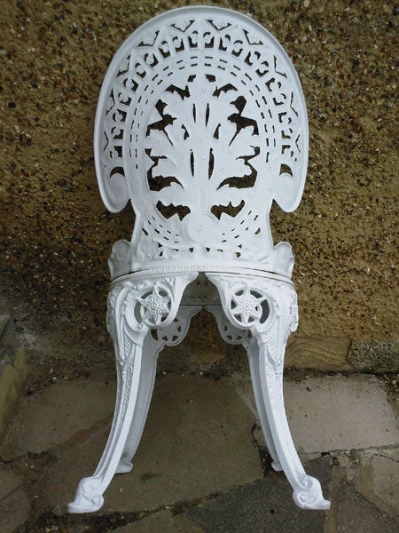 White ornate cast iron chair against a concrete wall.White ornate metal chair against a concrete wall.