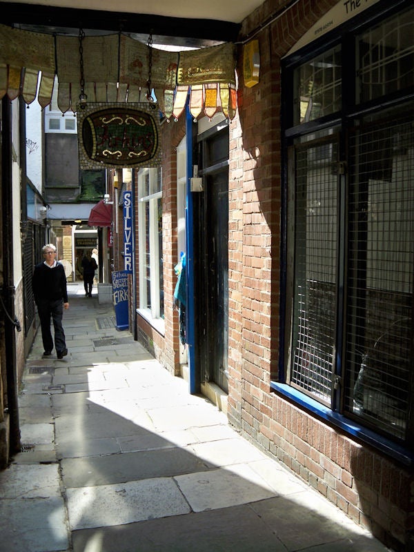 Man walking down a sunny, narrow street with shopsSunny alleyway shot with Kodak V1073 camera.