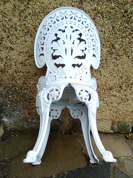 White ornate metal chair against a textured wallWhite ornate metal garden chair against a wall.