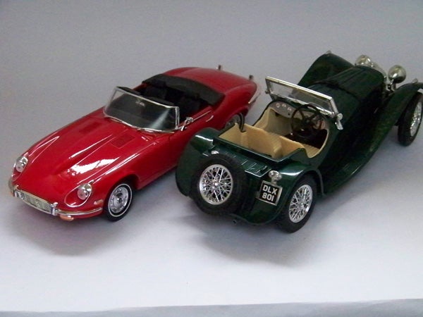 Toy model cars, red and green, photographed on a light background.Two model vintage cars on a white surface.