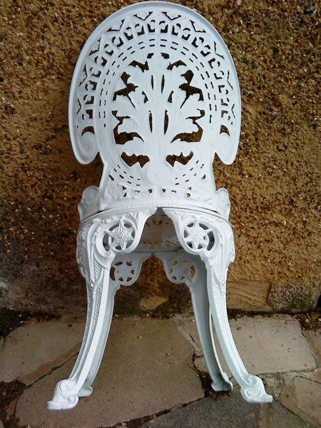 White ornate metal chair against a brick wall.White vintage ornate metal chair against a wall
