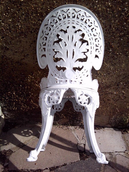 White ornate iron chair against a textured wall.White ornate garden chair against a concrete wall.