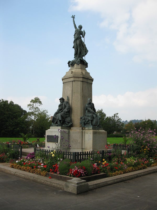 War memorial statue surrounded by colorful flowers in a park.Statue with flowers in a park on a cloudy day.