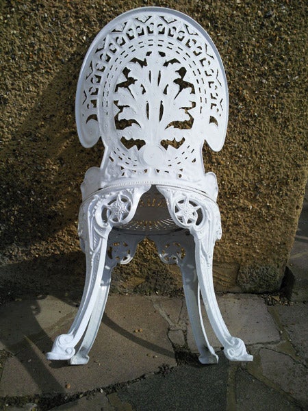 Ornate white cast iron garden chair against a stone wall.Intricately designed white vintage chair outdoors.