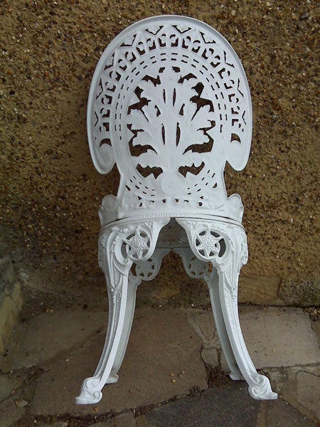 White ornate cast iron garden chair against a wall.