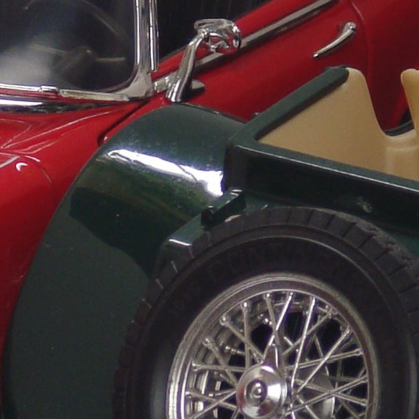 Close-up of a red and green toy car wheel and side mirror.