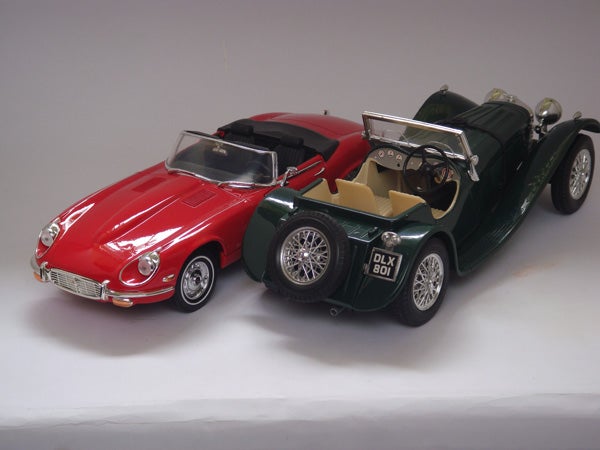 Two model cars, a red and a green vintage convertible.