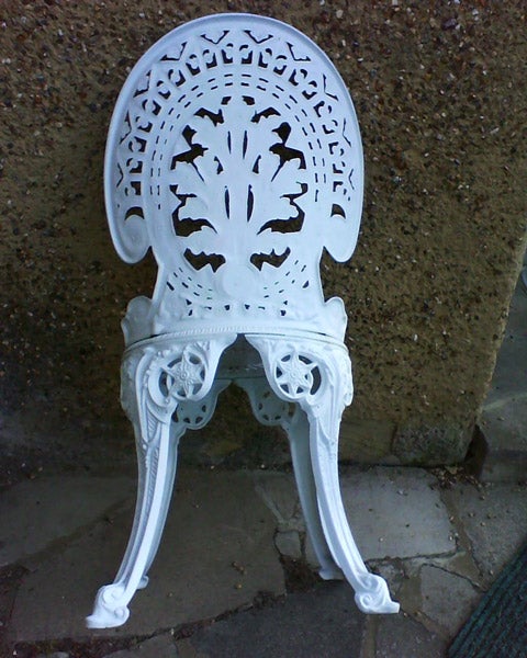 White ornate metal chair against a concrete wall.