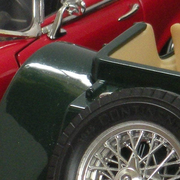 Close-up of a vintage red and green toy car wheel and fender.