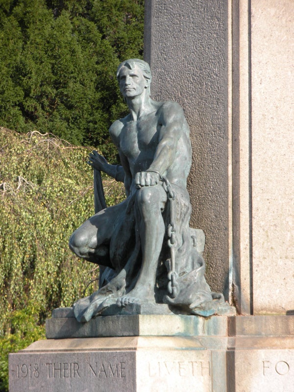 Bronze statue of a seated man with chains on his feet.