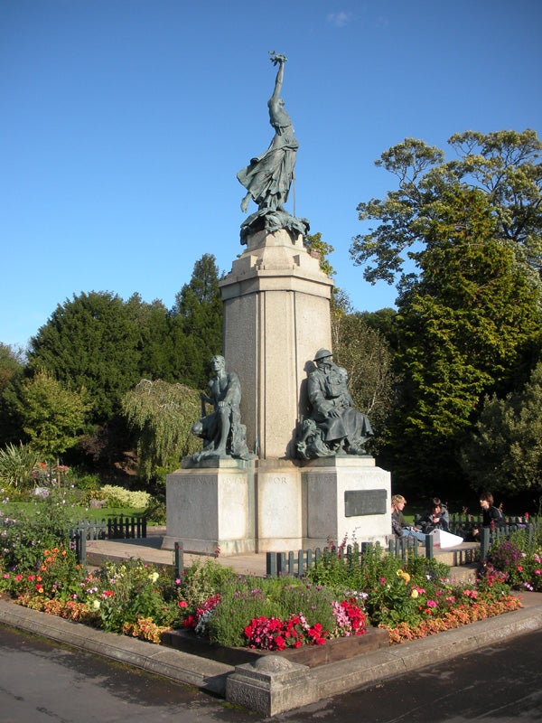 Statue surrounded by flowerbeds under clear blue sky.