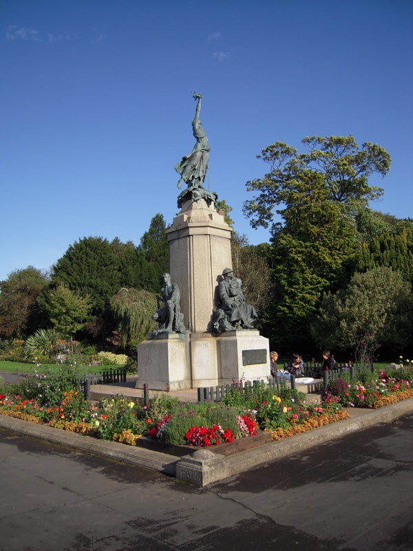 War memorial statue surrounded by colorful flowerbeds in a park