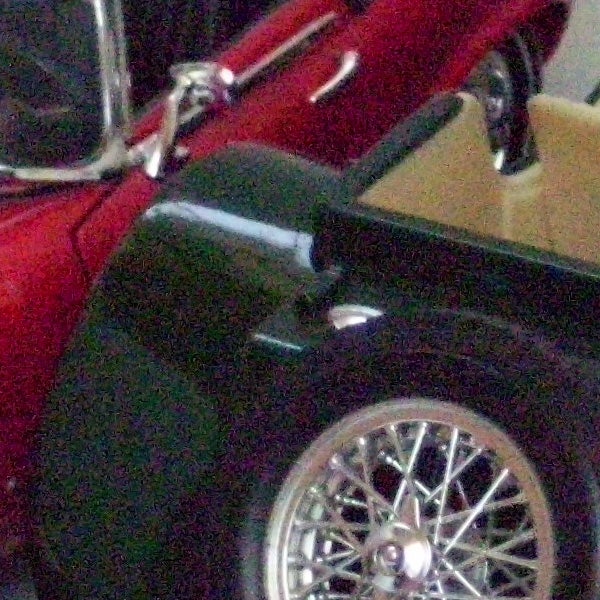 Low-resolution photo of a classic red car's side and wheel.