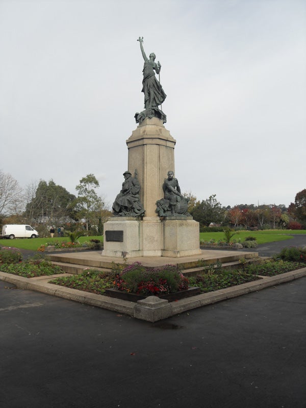 War memorial statue in a landscaped park setting.