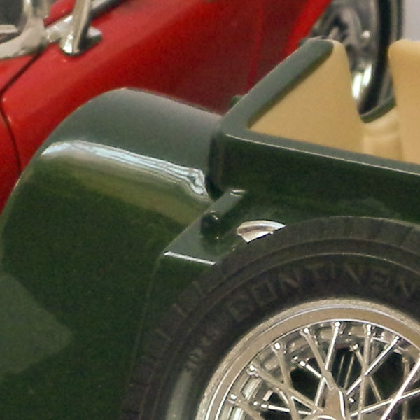 Close-up of green vintage car wheel and red bodywork.