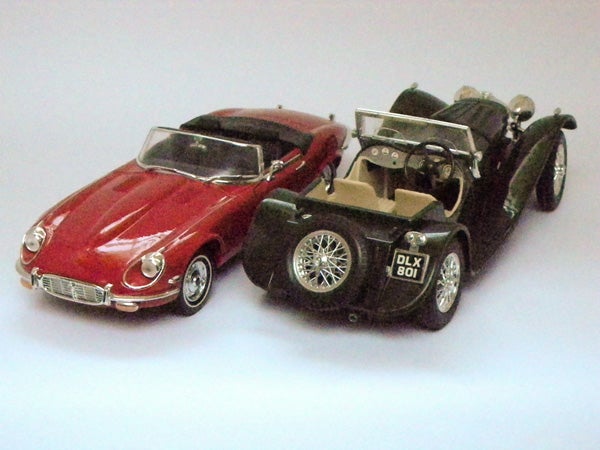 Two vintage model cars on a grey surface.
