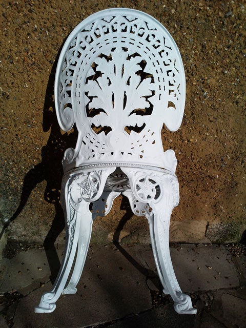 White ornate metal chair against a concrete background.