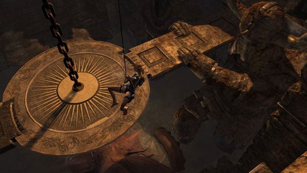 Lara Croft hanging from a chain in an ancient tomb.