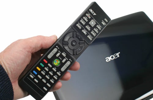 Hand holding remote control in front of Acer Aspire 6935G laptop.