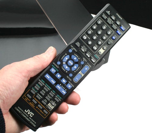 Hand holding a JVC NX-F7 system remote control.