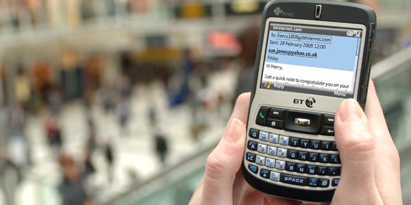Hand holding a BT branded smartphone with email on screen.